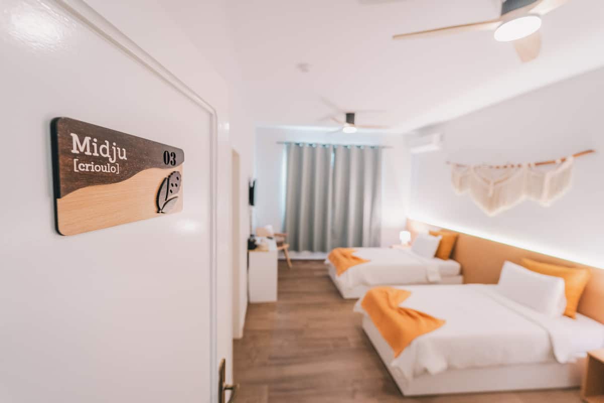 Habitación de hotel con dos camas, un escritorio, una silla y una ventana con cortinas.