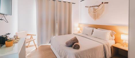 A modern hotel room with a bed, bedside tables, a desk, and a television.
