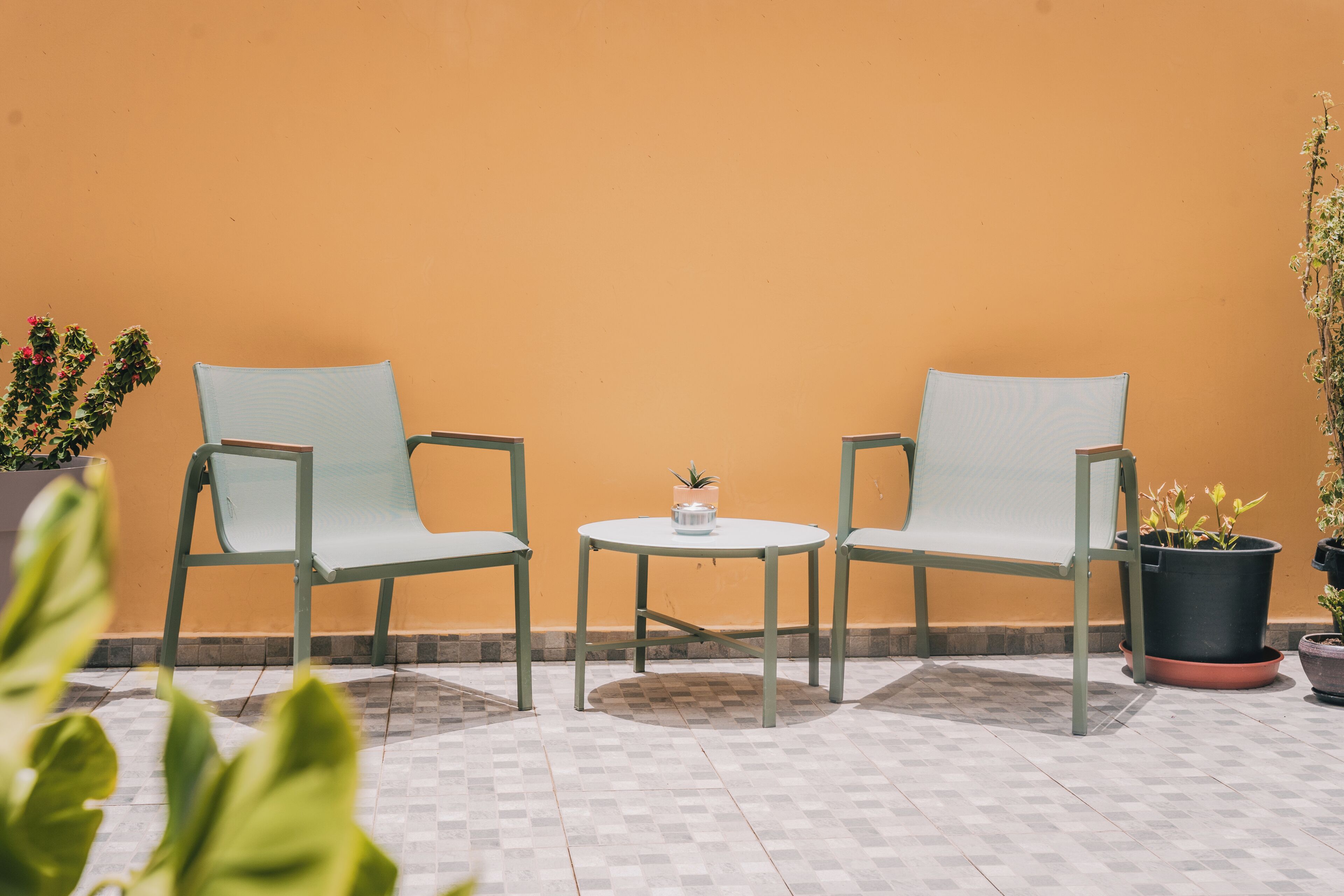 Two chairs and a small table in a patio area with a tiled floor and potted plants.