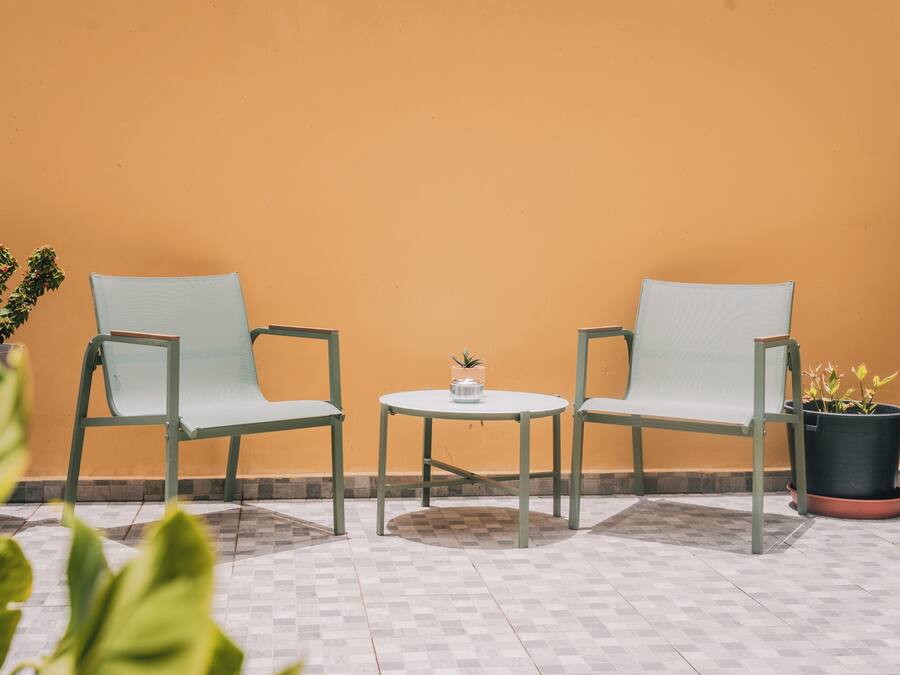 Dos sillas y una mesita en un patio con suelo de baldosas y plantas en macetas.