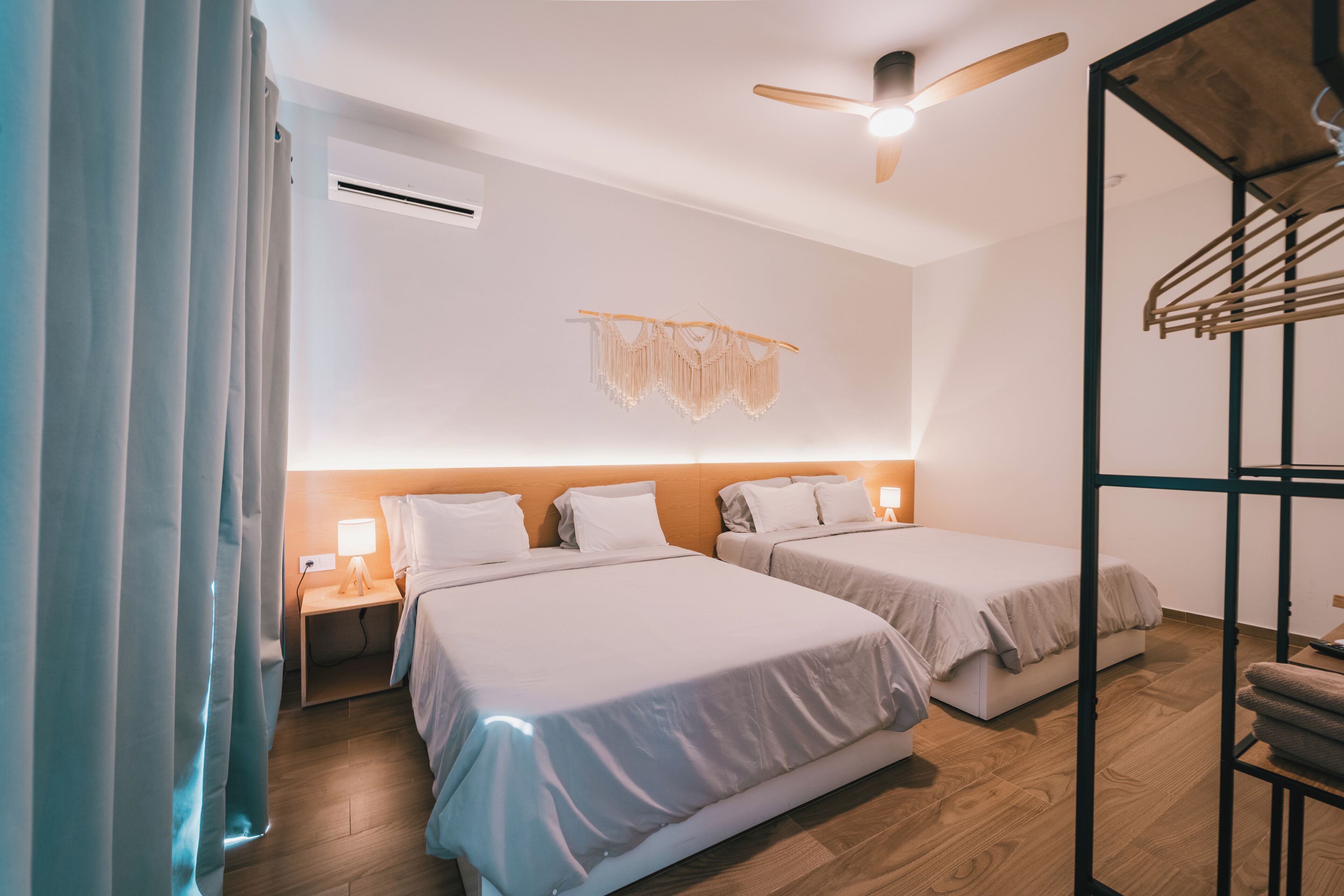 Hotelkamer met twee bedden, een plafondventilator, een airconditioningapparaat, een wandlamp en een houten vloer.