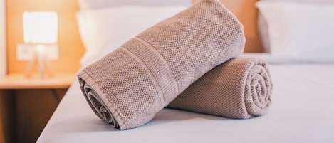 En snyggt bäddad säng med en hoprullad, beige handduk på den.