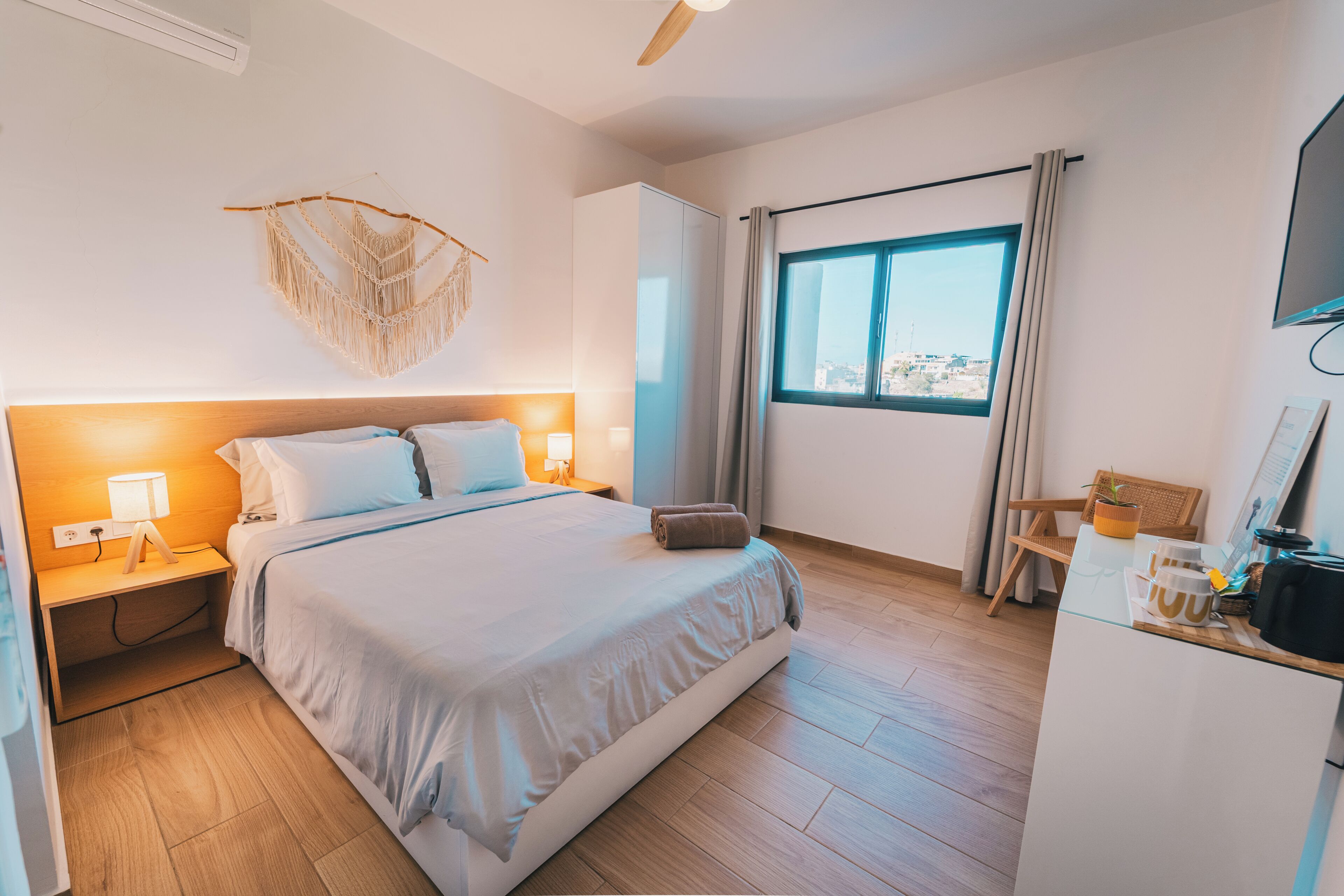 Une chambre d’hôtel comprenant un lit, une table de chevet, une lampe, une armoire, une fenêtre et un petit coin cuisine.