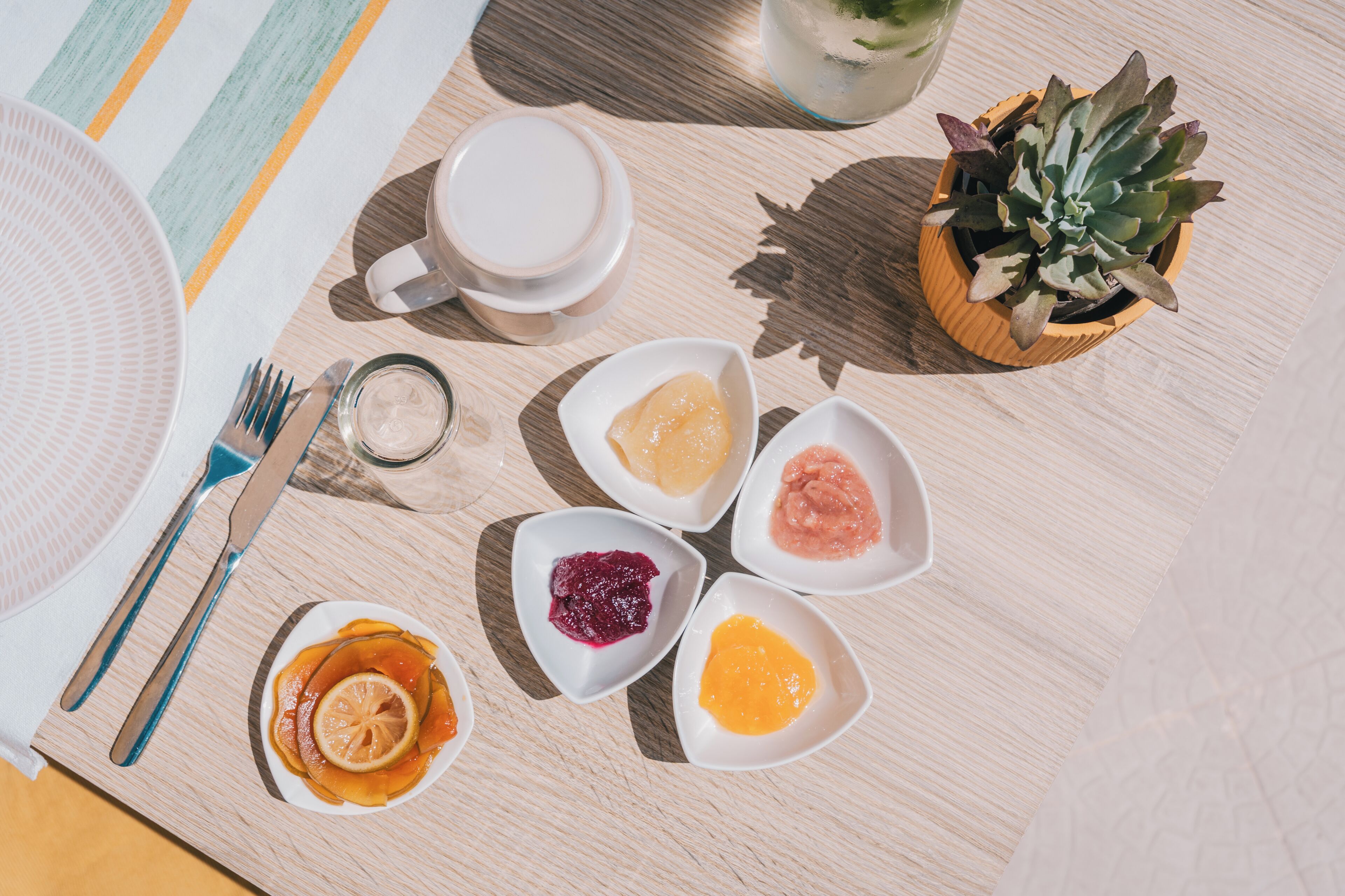 A table with a plate of food, a cup, a small potted plant, and a glass of water.