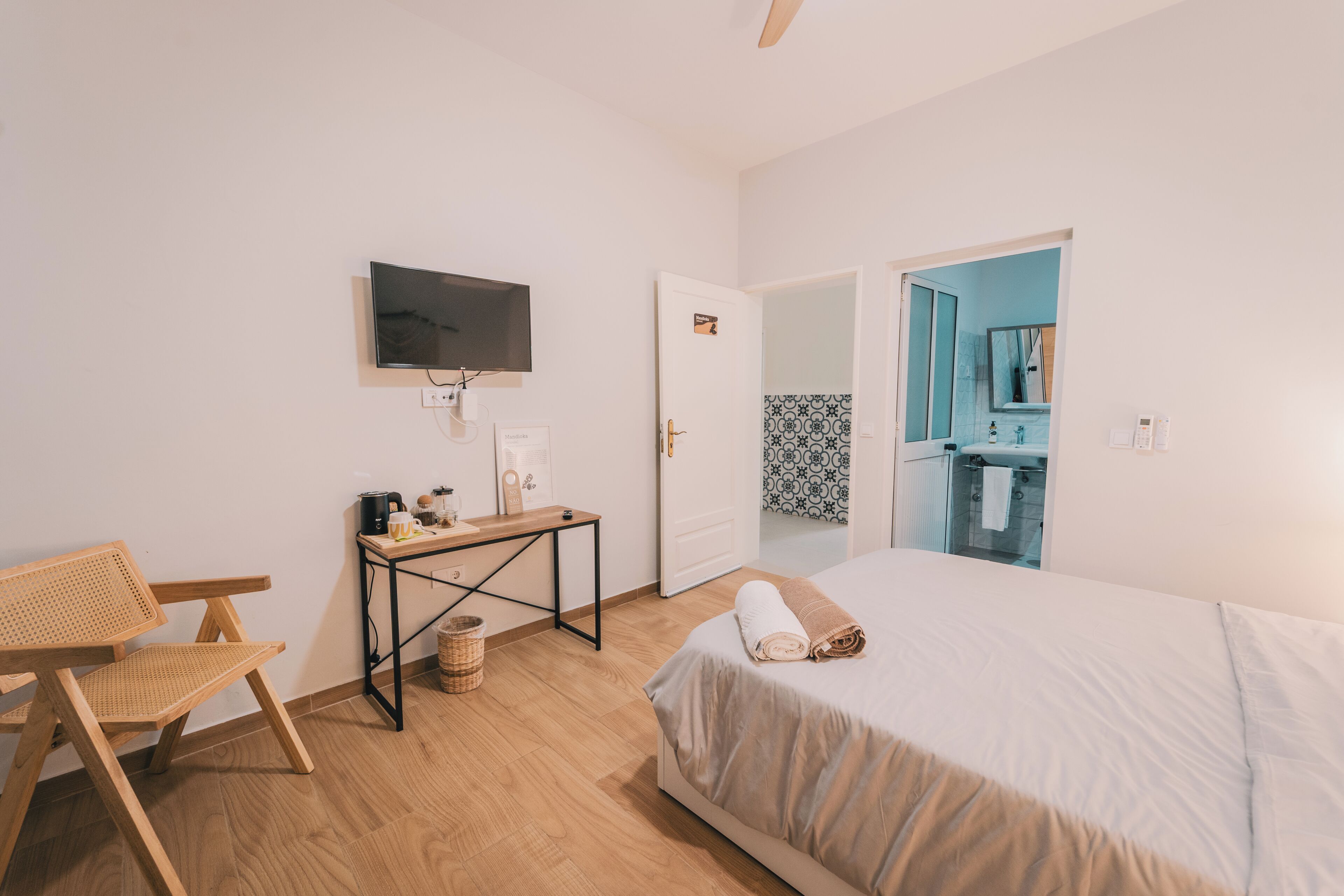 Un dormitorio con cama, escritorio, silla, televisor y baño visible a través de una puerta abierta.