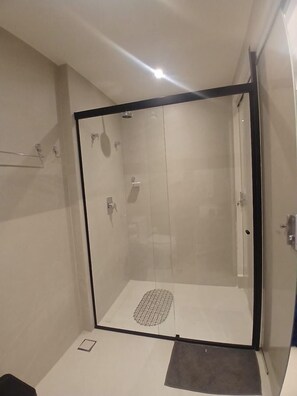 Une salle de douche fermée par des parois de verre, dotée d’un sol carrelé, d’une pomme de douche et d’un porte-serviettes.