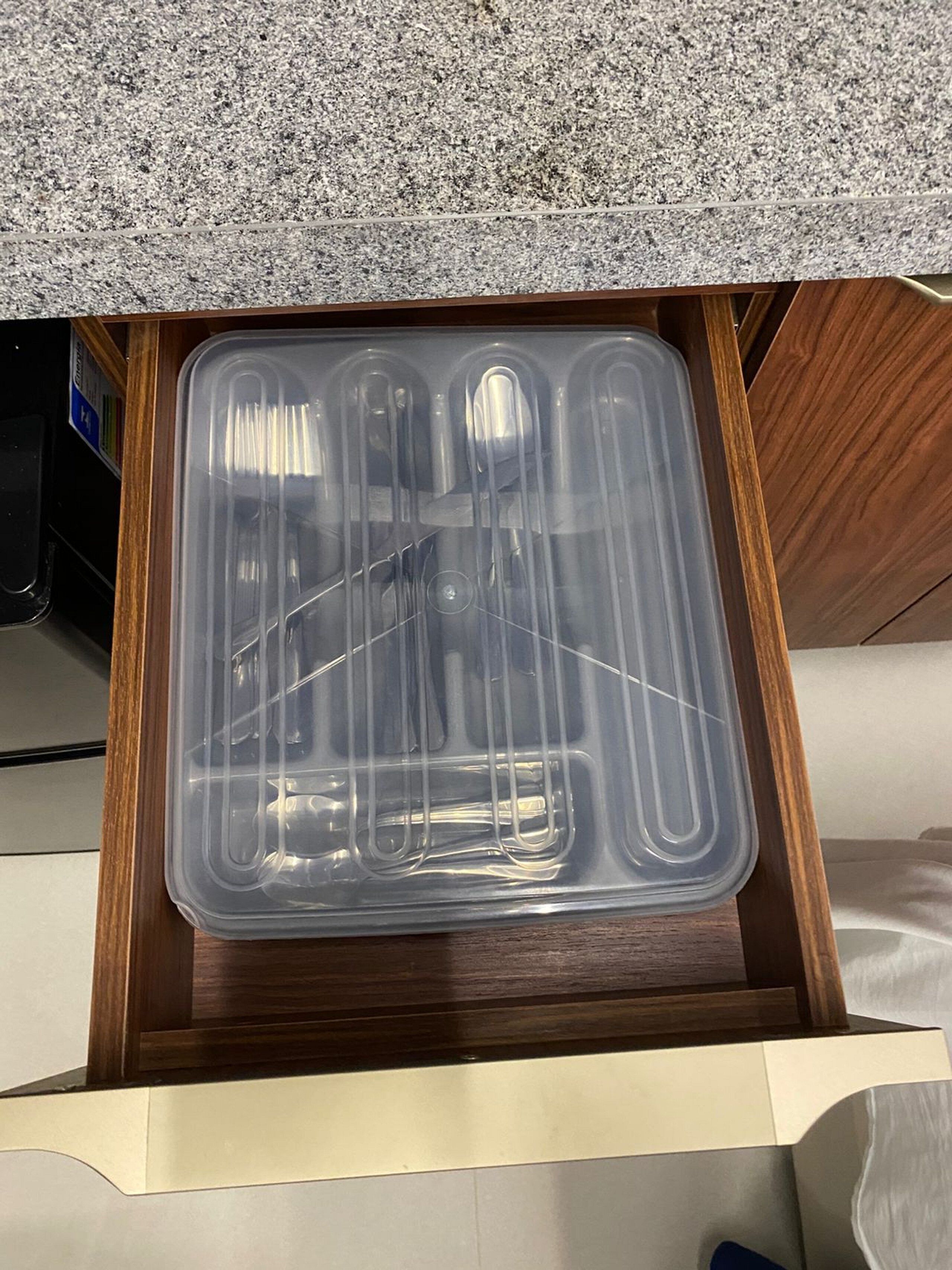 A drawer with a clear plastic container holding utensils.