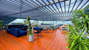 Un vaste salon extérieur doté d’un plancher en bois, de sièges bleus et de plantes en pot.