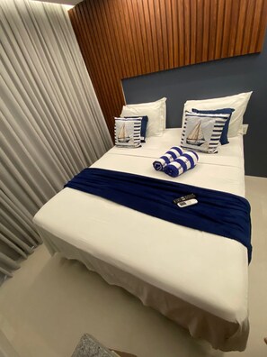 Un lit bien fait, avec un oreiller à rayures bleues et blanches, une couverture bleue et une télécommande posée sur le lit.