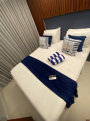 Una cama bien hecha con una colcha azul, almohadas blancas y almohadas a rayas con diseños de veleros.