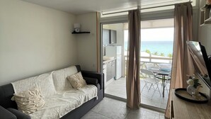A modern living room with a dark sofa, a wooden side table, and a view of the ocean through a glass door. - Studio with pool access and views of the Diamond Rock and Morne Larcher (Le Diamant)