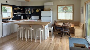 Une cuisine moderne avec un îlot central, des chaises blanches, une table à manger et une vue sur l’extérieur.