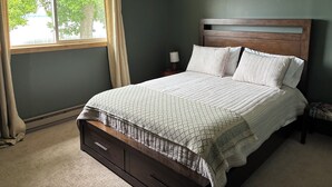 Une chambre à coucher comprenant un lit, une table de chevet, une lampe, une fenêtre avec des rideaux et un appareil de climatisation.