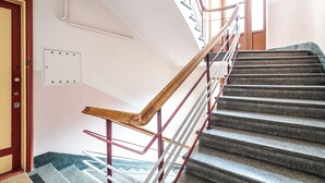 A staircase with a wooden handrail and metal balusters, leading to a landing with a door and a light switch on the wall. - RentPlanet - Apartament Sobieskiego (Kraków)