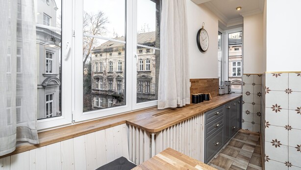 A modern kitchen with large windows, wooden countertops, and a view of historic buildings. - RentPlanet - Apartament Sobieskiego (Kraków)