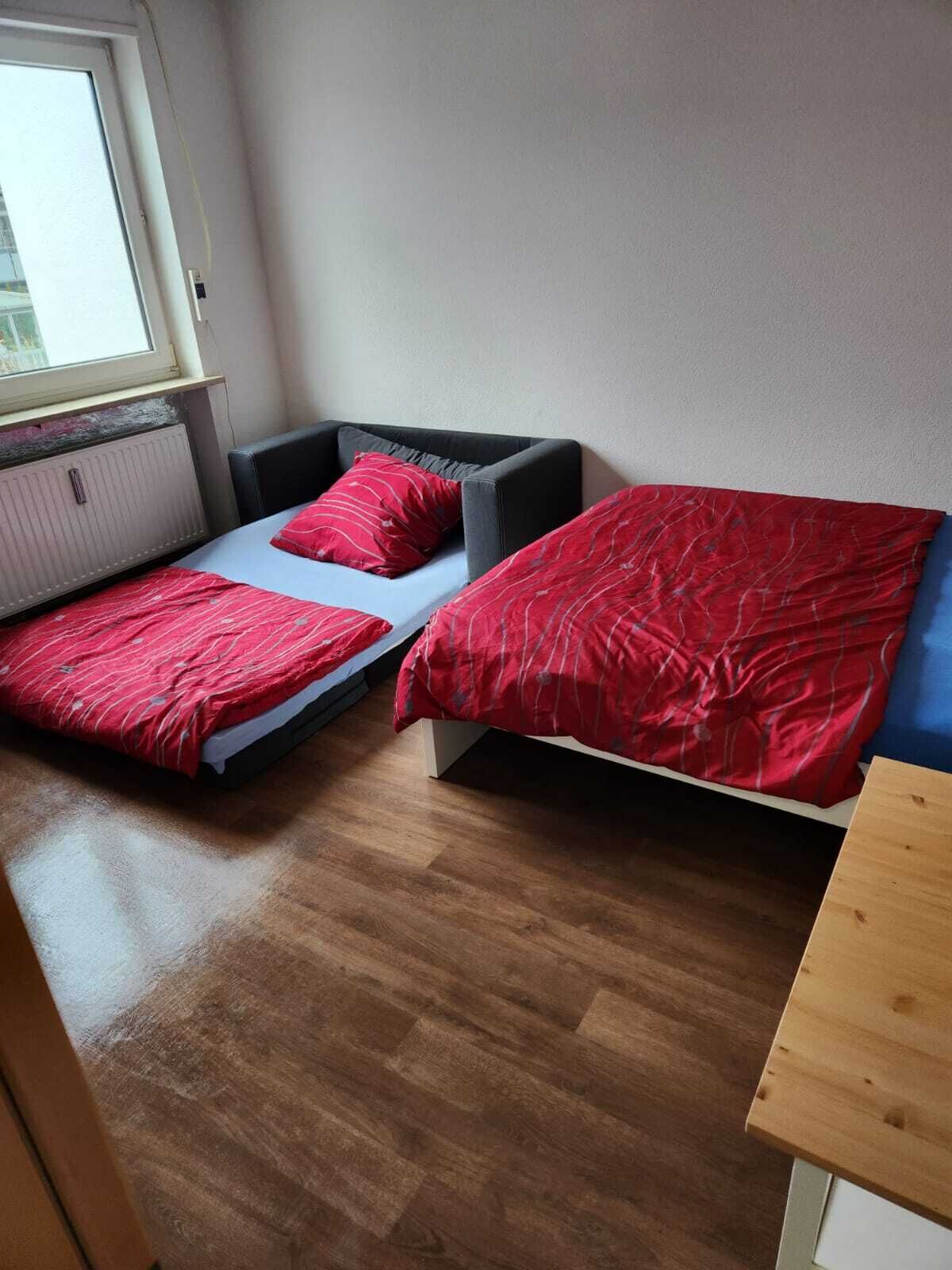 Una habitación pequeña con dos camas, cada una con ropa de cama roja, una ventana y un radiador.