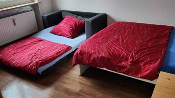 Una habitación pequeña con dos camas, cada una con ropa de cama roja, una ventana y un radiador.