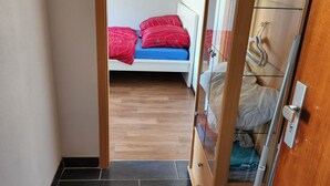 A narrow hallway leading to a bedroom with a bed, a wardrobe, and a vacuum cleaner. - Einfache 1-Zimmer Wohnung (Bad Woerishofen)
