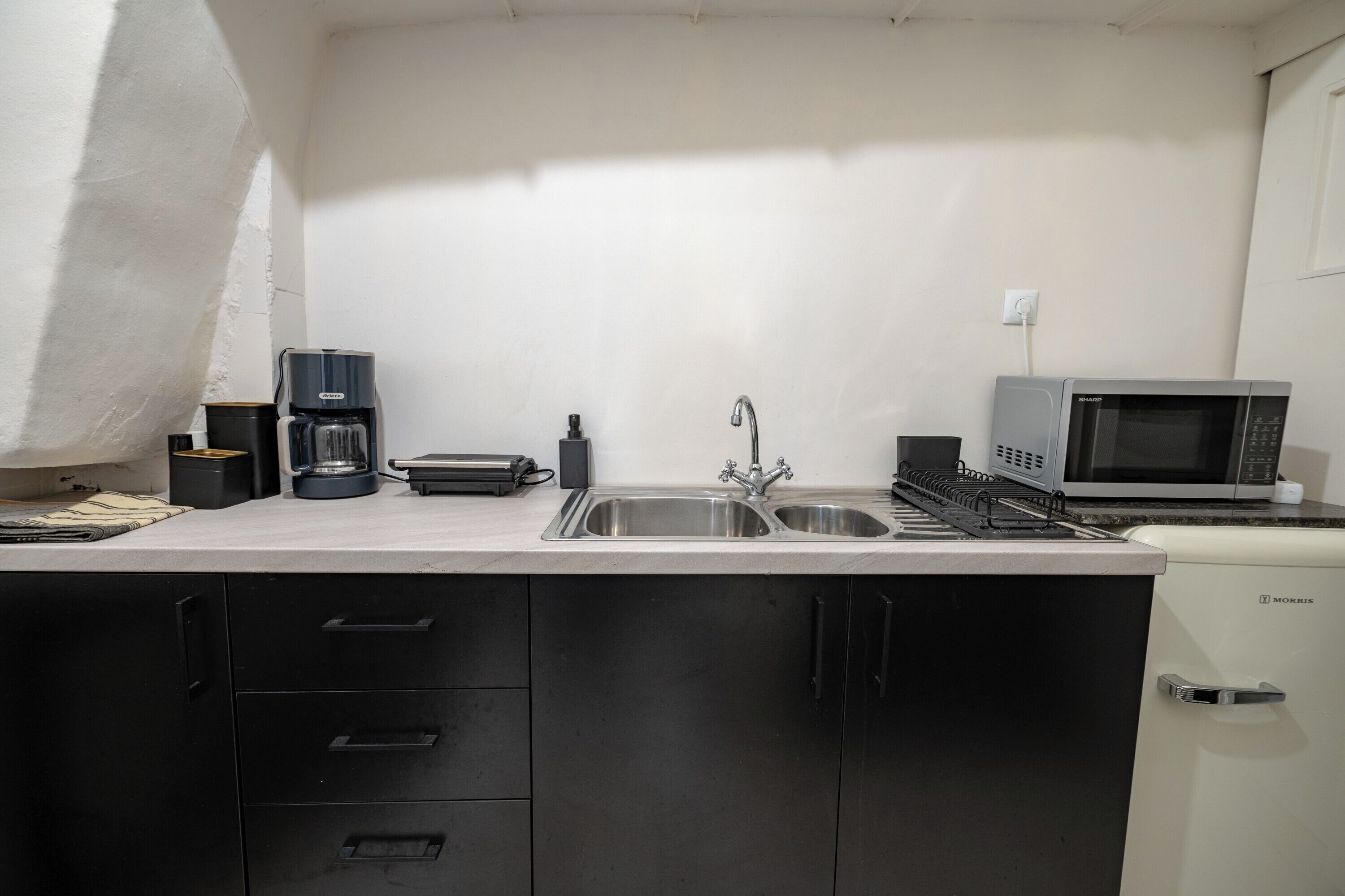 A compact kitchen with a sink, a coffee maker, a toaster, and a microwave.
