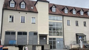 Ein mehrgeschossiges Gebäude mit einem zentralen Eingang, großen Fenstern und einem Parkplatz.