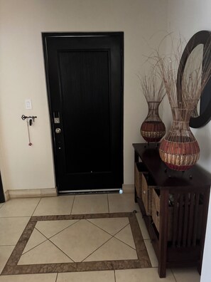 A black door with a keyhole and a lock, a small wall-mounted light switch, and a decorative vase on a wooden console table. - Stunning 2-Story Penthouse Tamarindo Guanacaste Costa Rica. Beach 2 Min Central (Tamarindo)