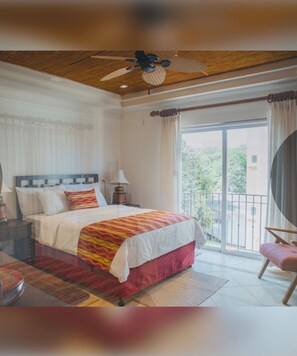A bedroom with a bed, a ceiling fan, a nightstand, a lamp, a chair, and a view of greenery outside. - Stunning 2-Story Penthouse Tamarindo Guanacaste Costa Rica. Beach 2 Min Central (Tamarindo)
