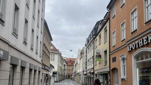 Una calle empedrada flanqueada por edificios históricos, entre ellos una farmacia.