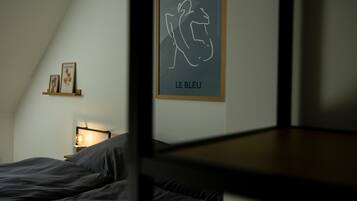 A bedroom with a bed, a bedside table with a lamp, and a framed artwork on the wall.