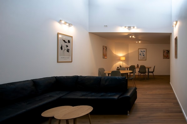 Ein modernes Wohnzimmer mit einem schwarzen Ledersofa, einem runden Couchtisch und einem Essbereich mit Tisch und Stühlen.