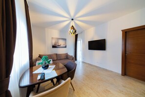 Een moderne woonkamer met een ronde eettafel, een bruine bank, een potplant en een aan de muur bevestigde televisie.