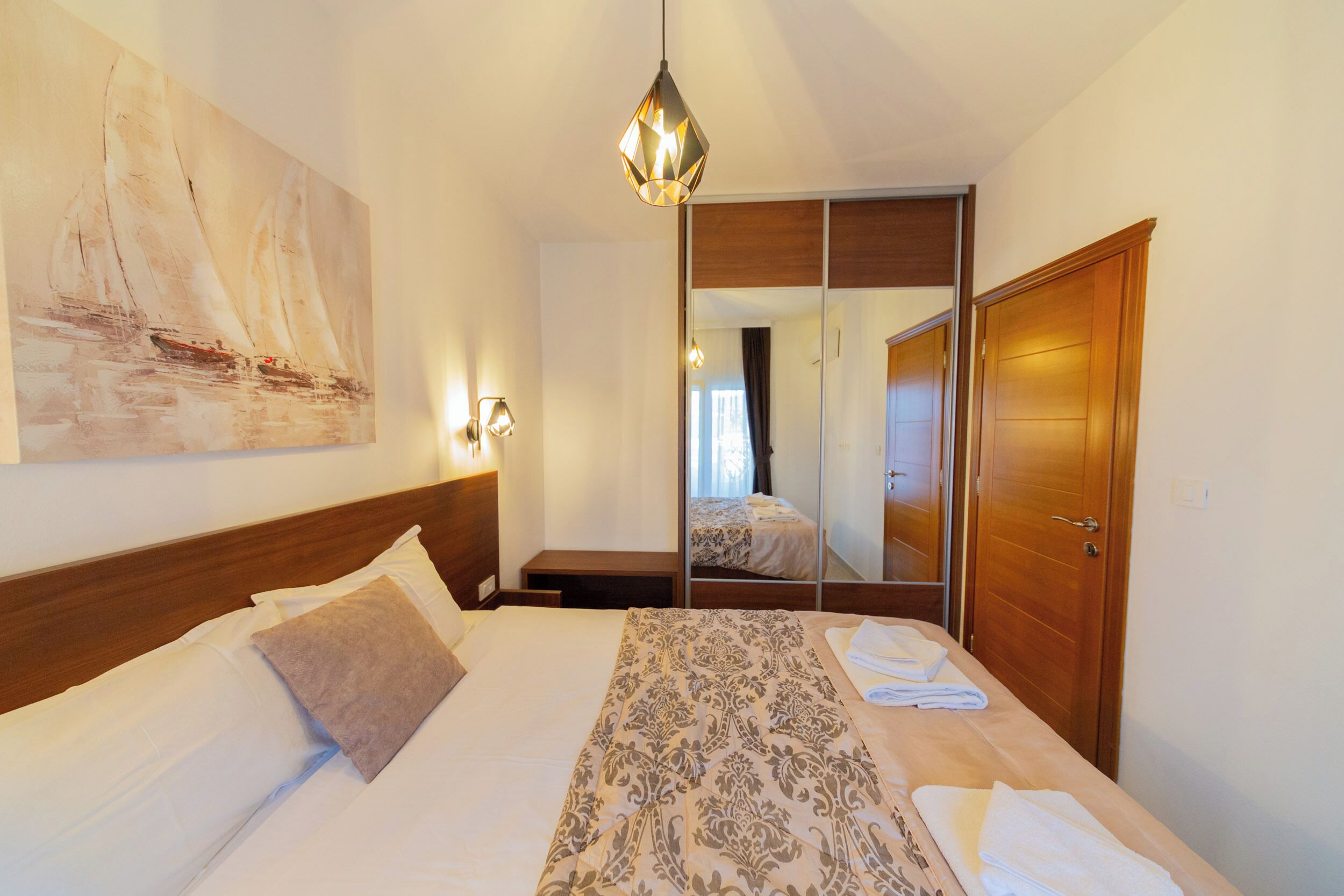 Une chambre d’hôtel avec un lit, une table de chevet, un miroir et une armoire en bois.