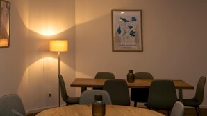 Een vergaderzaal met een ronde tafel, stoelen, een lamp en een ingelijst kunstwerk aan de muur.