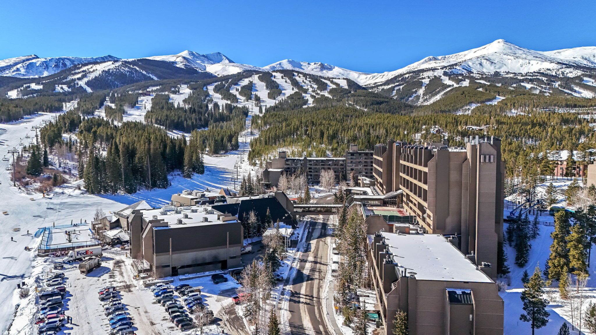 Une station de ski avec un parking, des bâtiments et, en arrière-plan, des montagnes enneigées.