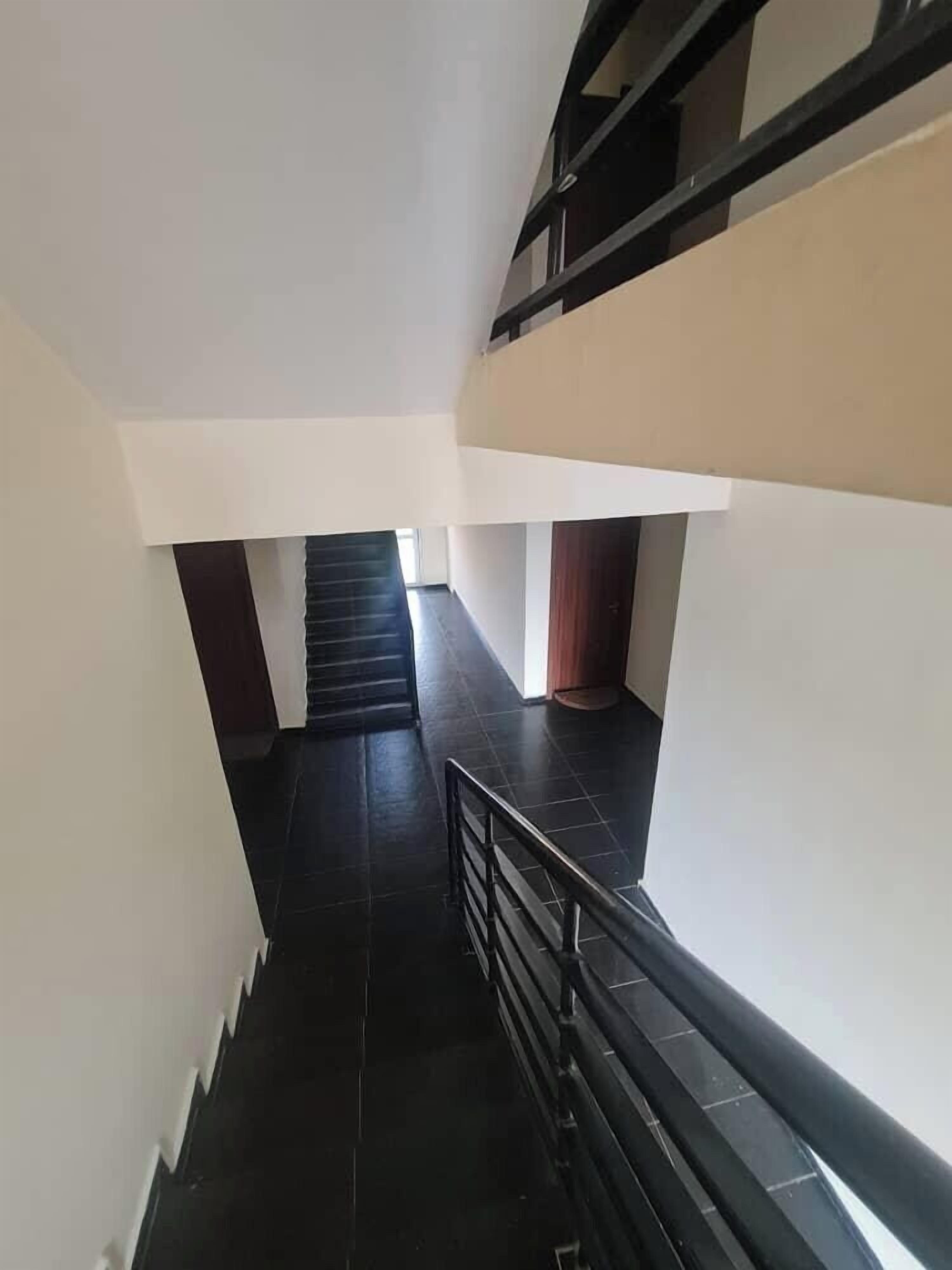 A narrow, tiled stairway with a black railing, leading to a higher floor.