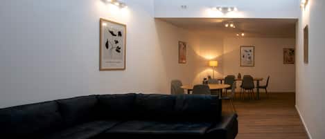 A modern living room with a black leather sofa, a round wooden coffee table, and a dining area with a table and chairs.