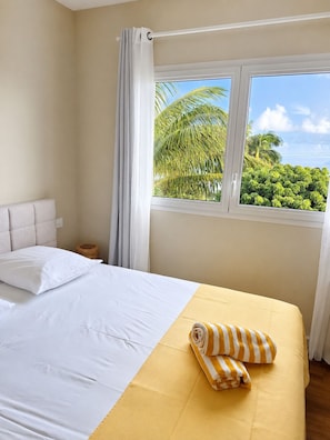 Ein Hotelzimmer mit Bett, Fenster und Blick auf Palmen.
