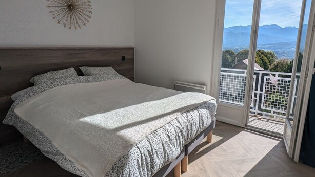 Ein Schlafzimmer mit einem großen Bett, einer Hängelampe, einem Wanddekor und einem Balkon mit Bergblick.