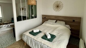 Ein Schlafzimmer mit einem großen Bett, einer gewebten Pendelleuchte, einem Wanddekor und Blick auf ein Badezimmer.