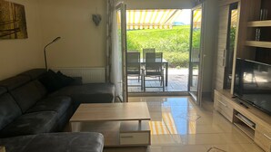 A modern living room with a sofa, coffee table, TV, and a sliding glass door leading to an outdoor patio. - Holiday Home 'Lechseeidylle' in Elevated Edge Location with 'Königscard' Benefit (Lechbruck am See)