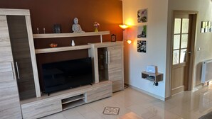A modern living room with a large TV, wooden entertainment unit, and a small table. - Holiday Home 'Lechseeidylle' in Elevated Edge Location with 'Königscard' Benefit (Lechbruck am See)