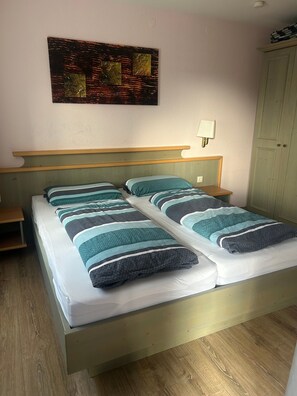 Een tweepersoonsbed met gestreept beddengoed, een nachtkastje, een wandlamp en een houten vloer.