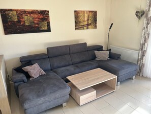 Een moderne woonkamer met een grijze modulaire bank, een houten salontafel en twee abstracte schilderijen aan de muur.