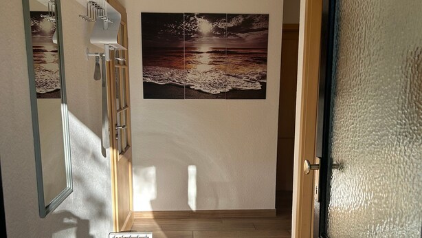 A hallway with a wooden floor, a door with frosted glass, a wall-mounted radiator, and a framed picture of a beach scene. - Holiday Home 'Lechseeidylle' in Elevated Edge Location with 'Königscard' Benefit (Lechbruck am See)