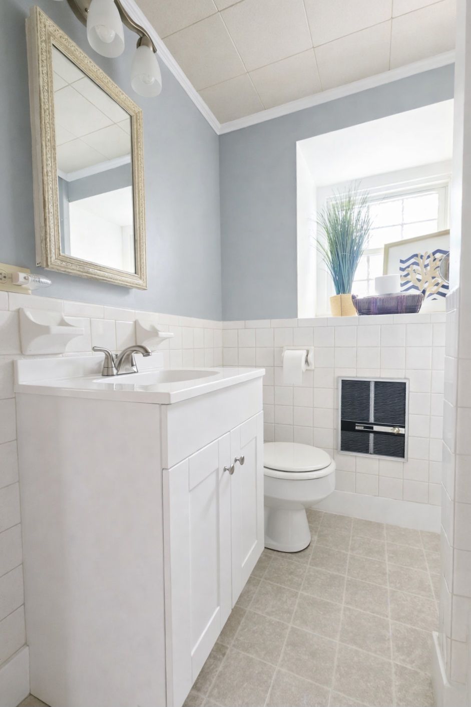 A bathroom with a white vanity, a mirror, a toilet, and a window with a plant.