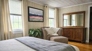 A bedroom with a bed, a chair, a dresser, a mirror, and a painting.