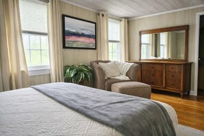 Ein Schlafzimmer mit Bett, Stuhl, Kommode, Spiegel und einem Gemälde.