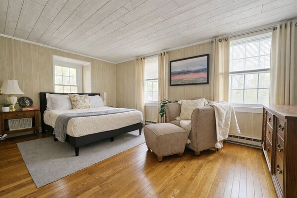 A bedroom with a bed, a chair, a nightstand, a dresser, and a window with curtains.