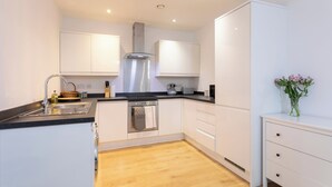 A modern kitchen with white cabinets, a stainless steel range hood, and a wooden floor. - The Albany Sleeps 2 With Wifi (Redhill)