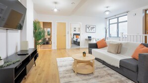 A modern living room with a sofa, coffee table, and TV. There is a door leading to another room and a plant in the corner. - The Albany Sleeps 2 With Wifi (Redhill)
