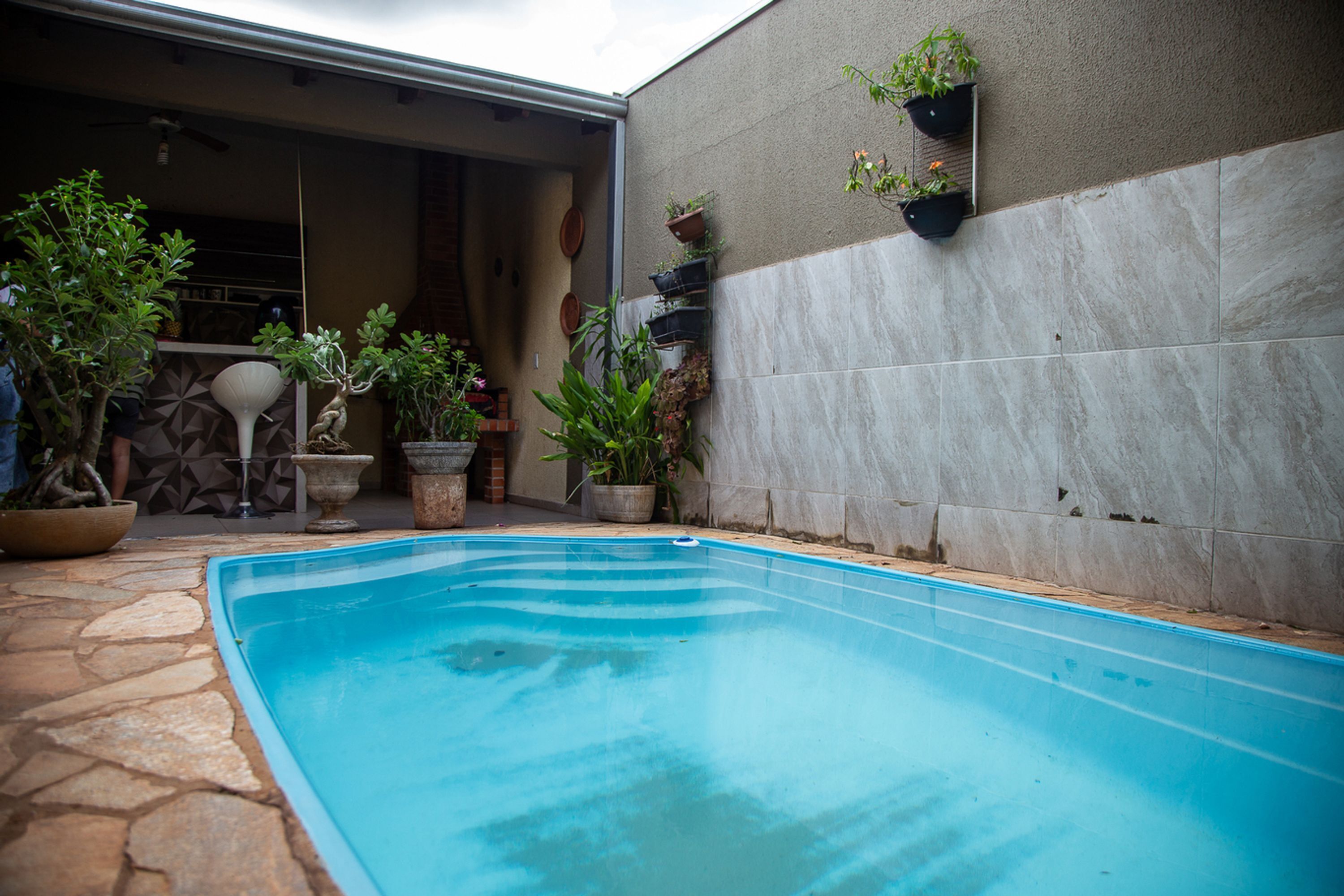 A swimming pool with stone tiles, surrounded by potted plants and a tiled wall.